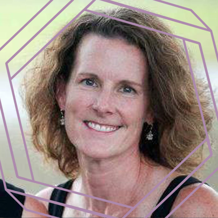 Randee, a white woman in her forties with wavy shoulder-length brown hair, smiles at the camera. There is a stylized purple hexagon framing the photo.