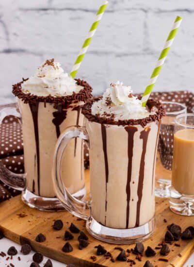 Two chocolate rimmed glass mugs containing frozen mudslide, whipped cream, and chocolate sauce.