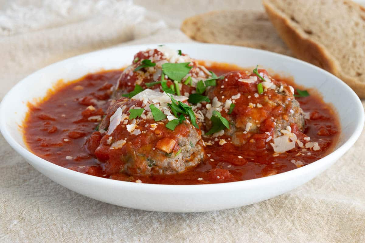 Three meatballs in a bowl with marinara sauce.