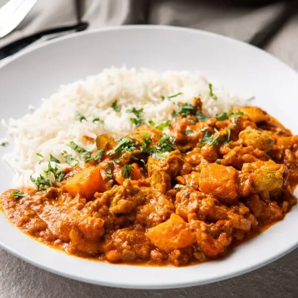 Side profile shot of the Butter Chicken with Basmati Rice, capturing the layers of creamy curry and fluffy rice. The focus is on the texture and rich color of the dish. The same grey countertop and dark grey cloth create a consistent and cozy background.