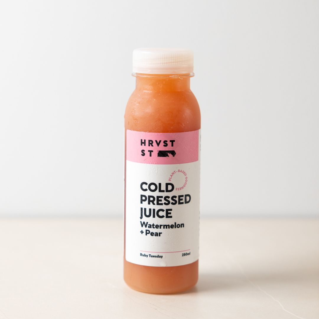 A full bottled serve of pink juice set against a white grey backdrop and bench.