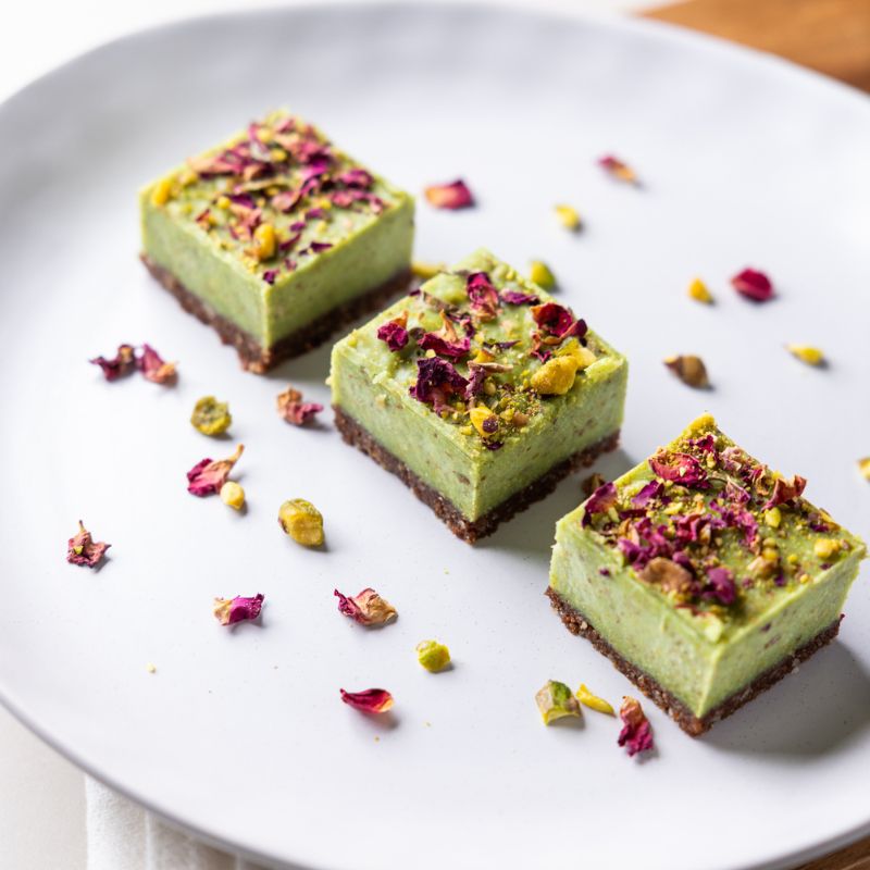 A close-up of three lime and pistachio slices, dusted with dried rose petals, sitting on a white plate.