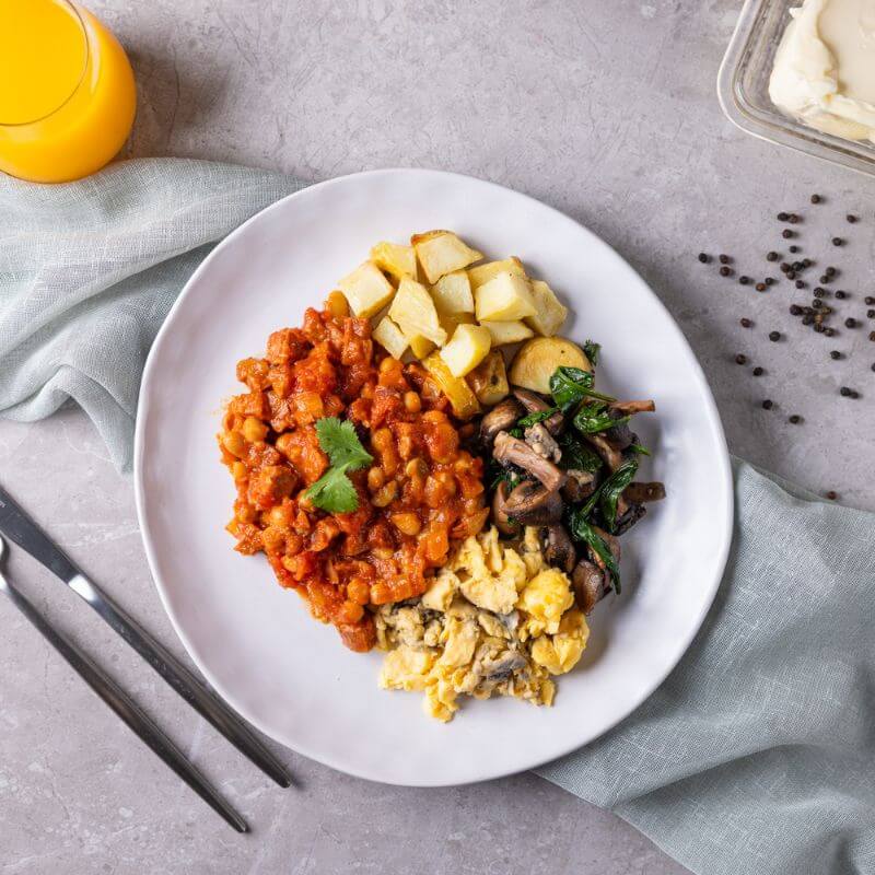 Flat lay shot of the All Day Big Breakfast on a white plate, showcasing chorizo, herby scrambled eggs, smoky baked beans, and crispy potato hash, all perfectly arranged.