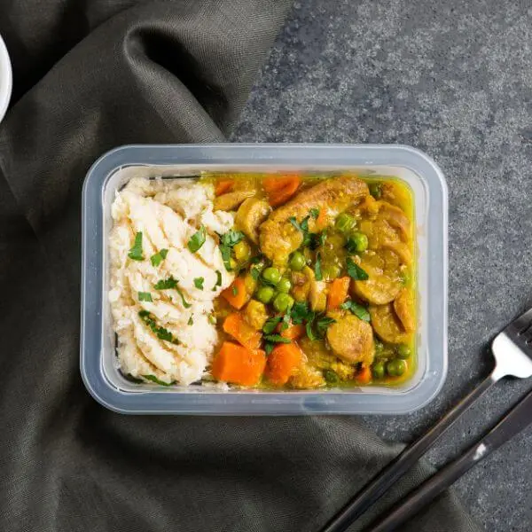 Container shot of curried sausage with white potato mash, focusing on the neat presentation in the container and providing a clean, minimalistic background for a professional shot.