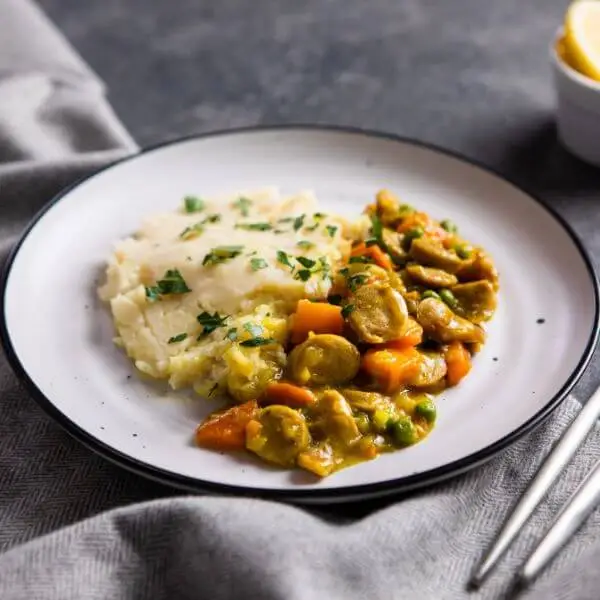 Side shot of the curried sausage with white potato mash, capturing the layers and textures of the dish while showcasing the comforting appearance of the creamy mash and curried sausage.