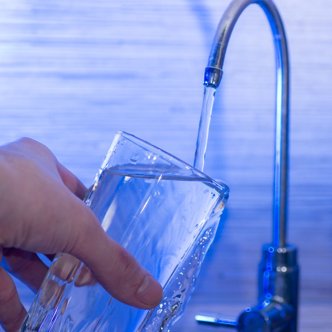 person pouring water from faucet into glass