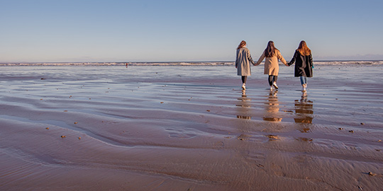 three students holding hands on beach