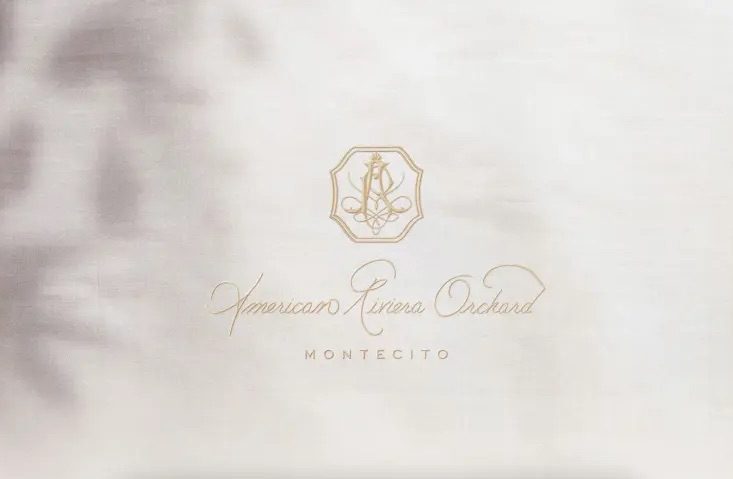 Meghan Markle introducing American Riviera Orchard jelly product with a white cloth background featuring gold text