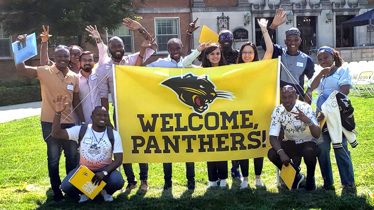 International students stand in front of Erskine Hall with a large banner that reads "Welcome Panthers"