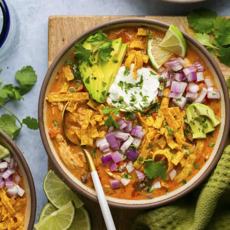 Soup topped with avocado, limes, onions, tortilla strips and cilantro.