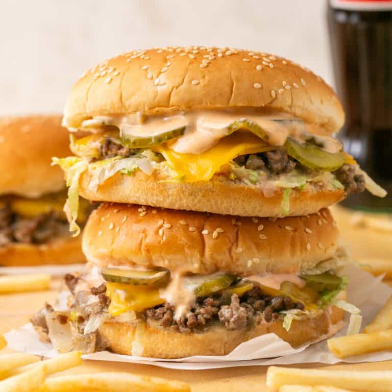 2 stacked sloppy joes with fries around and a coke in the background.