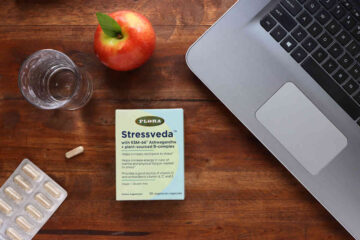 A box of Stressveda ksm-66 ashwagandha on a table with a laptop, water, and apple.