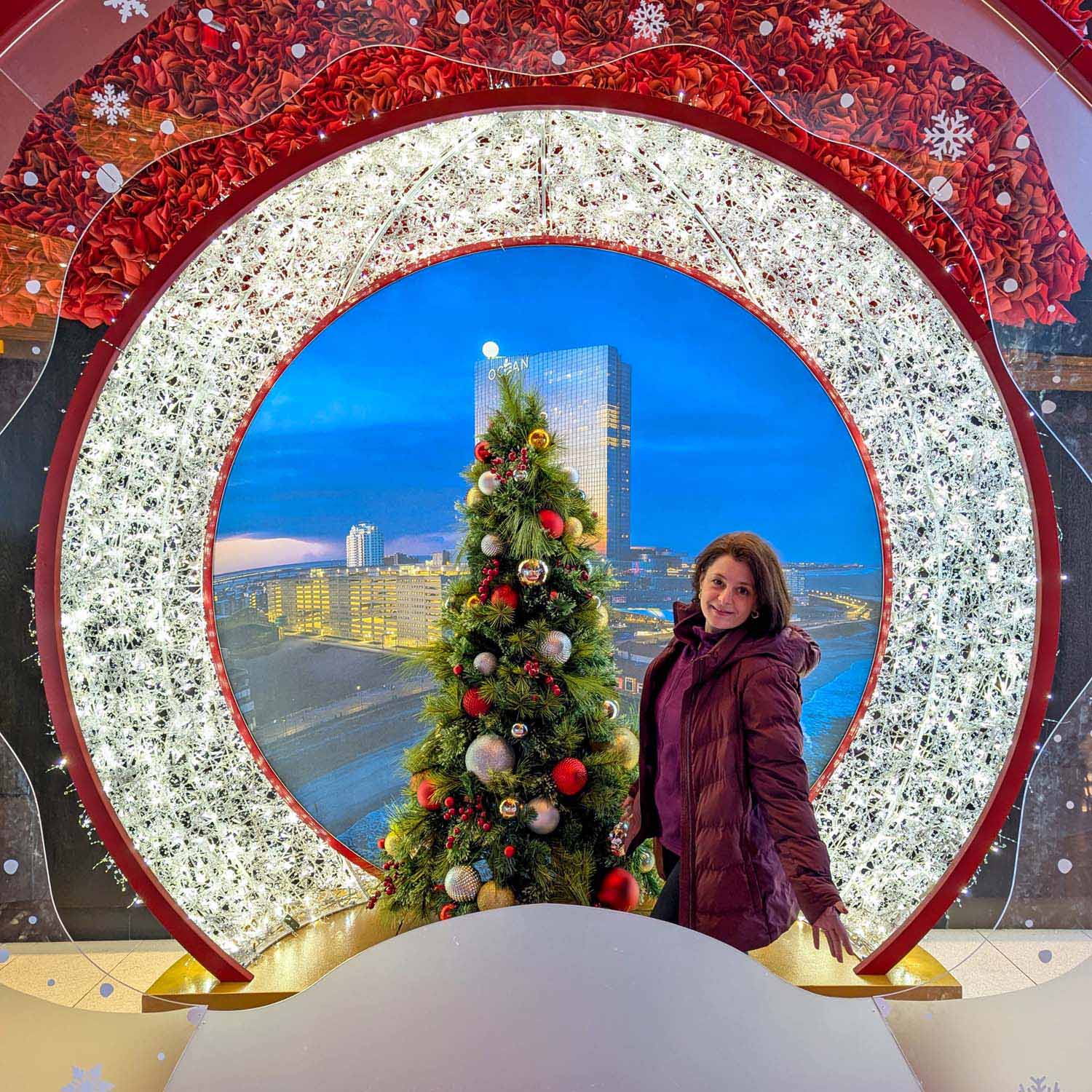 Circular light-up photo arch with white twinkling lights, decorated Christmas tree, and Ocean Casino Resort tower visible in the background