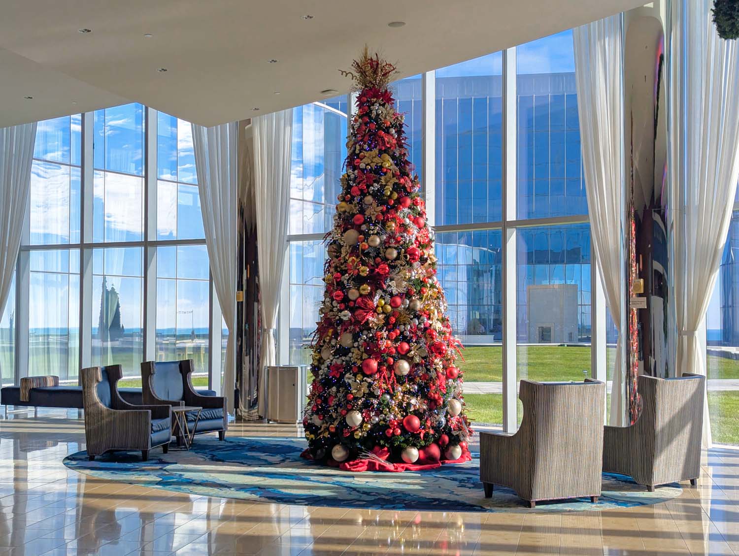 Massive Christmas tree decorated with red and gold ornaments in Ocean's lobby, surrounded by floor-to-ceiling windows and modern seating area