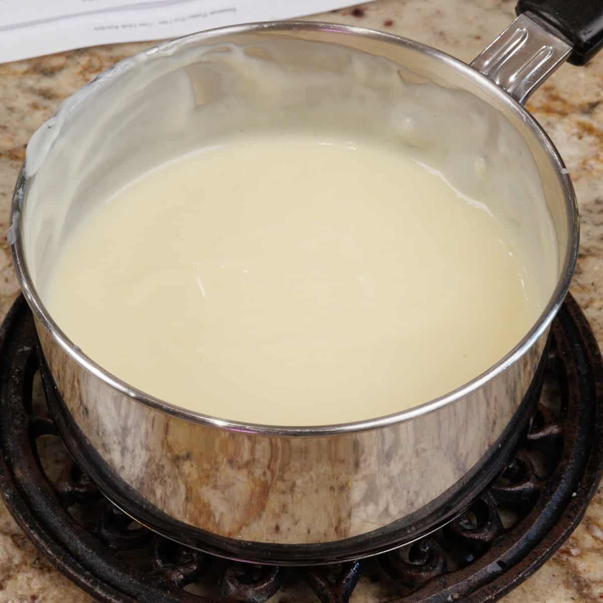 vanilla pudding in a small pot cooking on a kitchen counter.