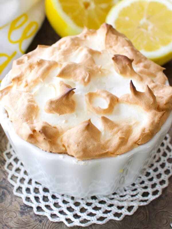 a small lemon meringue pie on a silver tray next to fresh lemons.