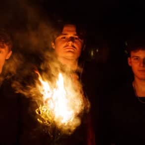 Three band members of 5 degrees north standing in the darkness holding a burning torch