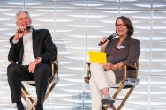 Andy and Susan North sit in folding chairs and hold microphones while smiling