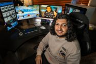 Muaaz Shakeel is seated at a computer desk with multiple monitors.