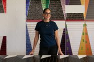 Dyani White Hawk stands with her large-scale, colorful work in an art studio.