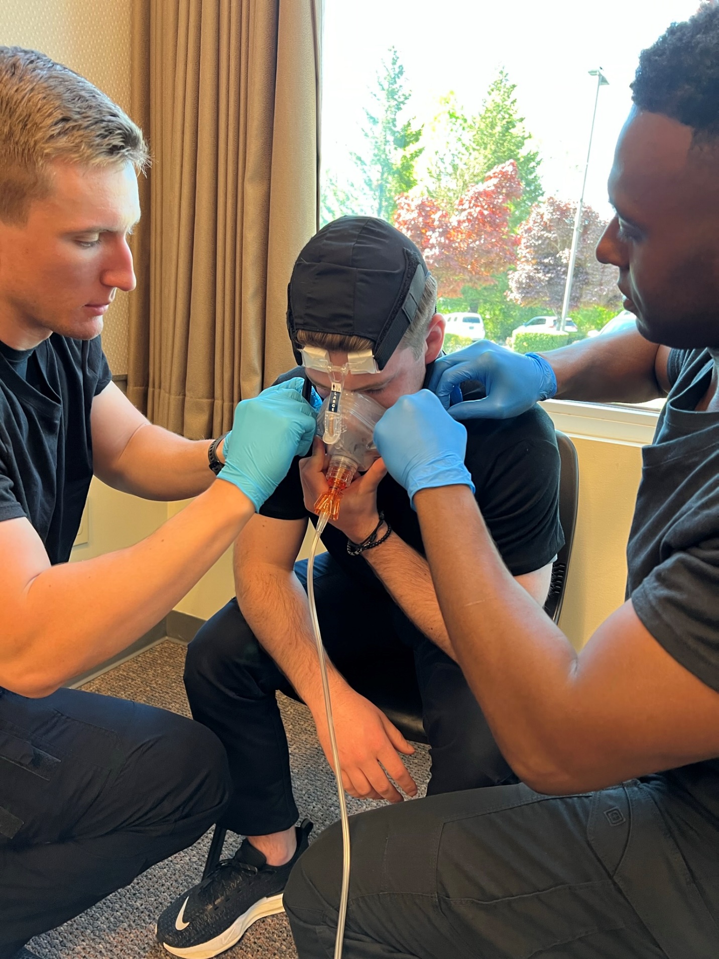 Two gloved EMTs securing CPAP straps to a seated patient.