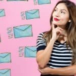 Woman with long hair and a striped shirt thoughtfully poses in front of a pink background decorated with illustrated envelopes, symbolizing communication and creativity.