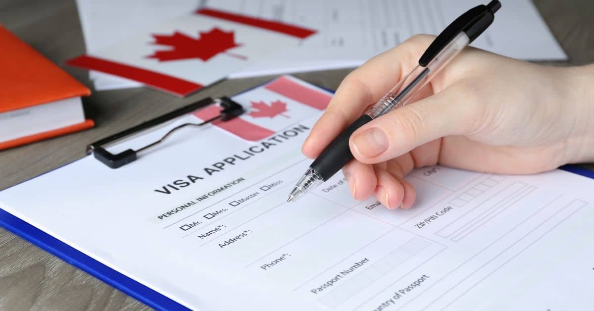 Hand filling out a Canadian visa application form with a pen, featuring a clipboard and Canadian flag in the background.