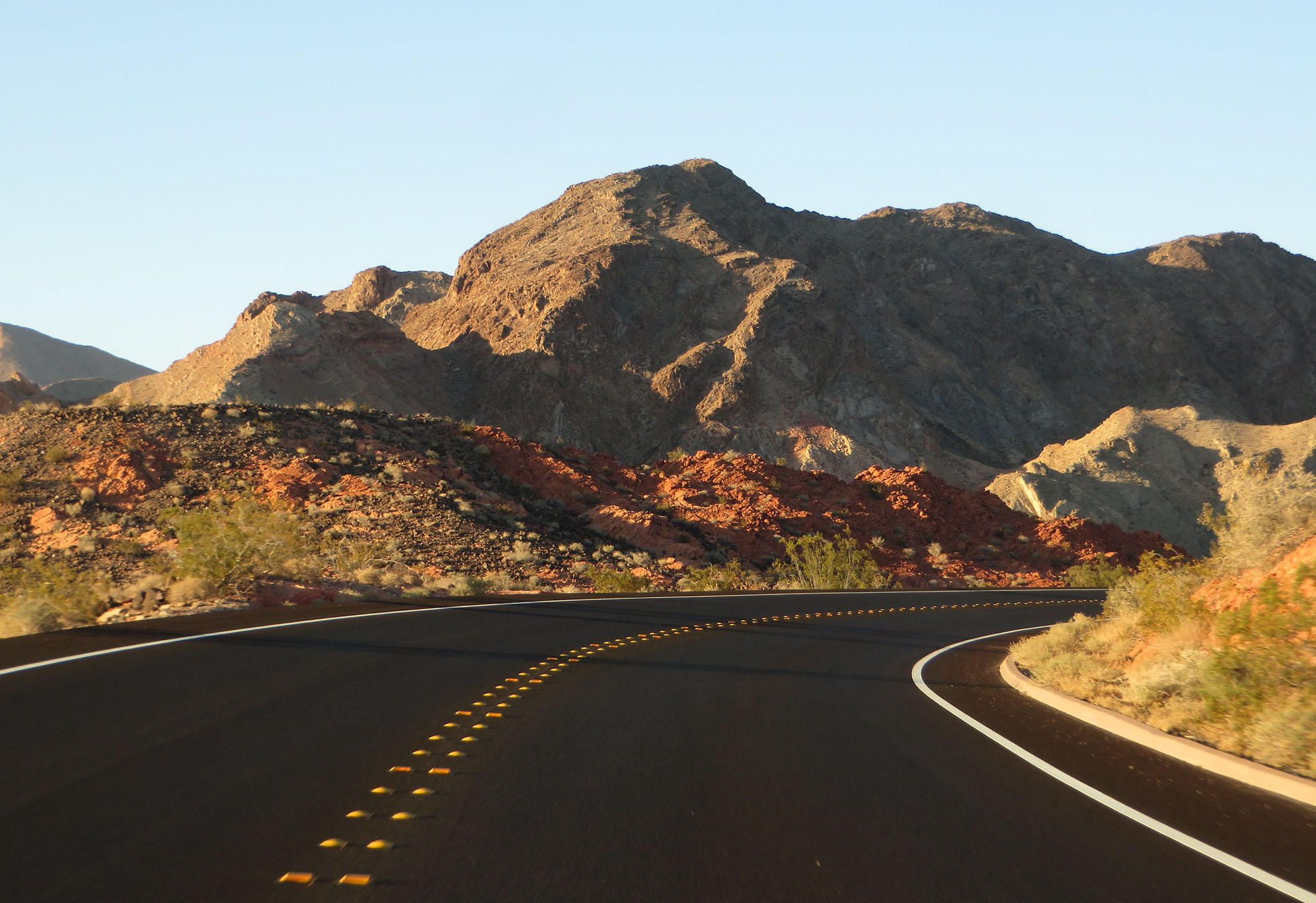 A curving road in front of a desert mountain ridge.