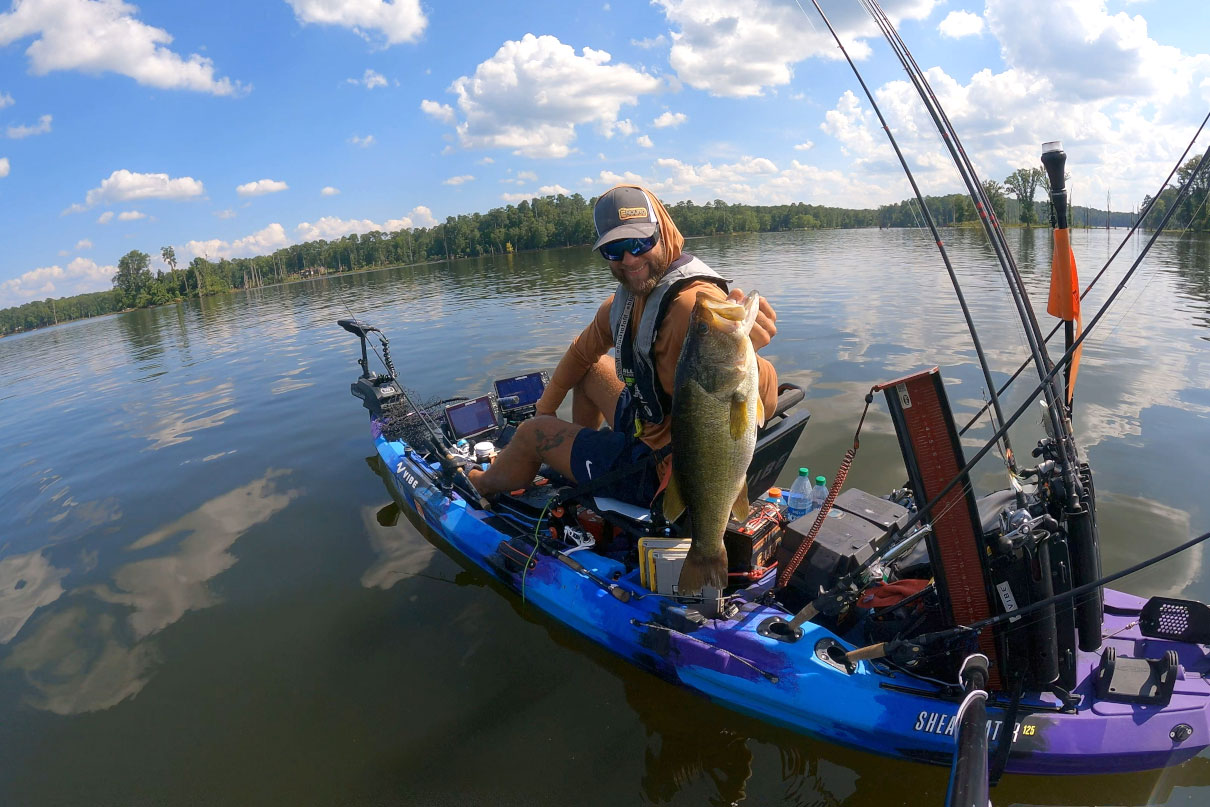 man holds up a large bass caught by kayak while fishing a with a bass rig