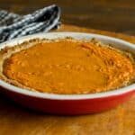 Pumpkin Pie in a red pie pan on a wood table