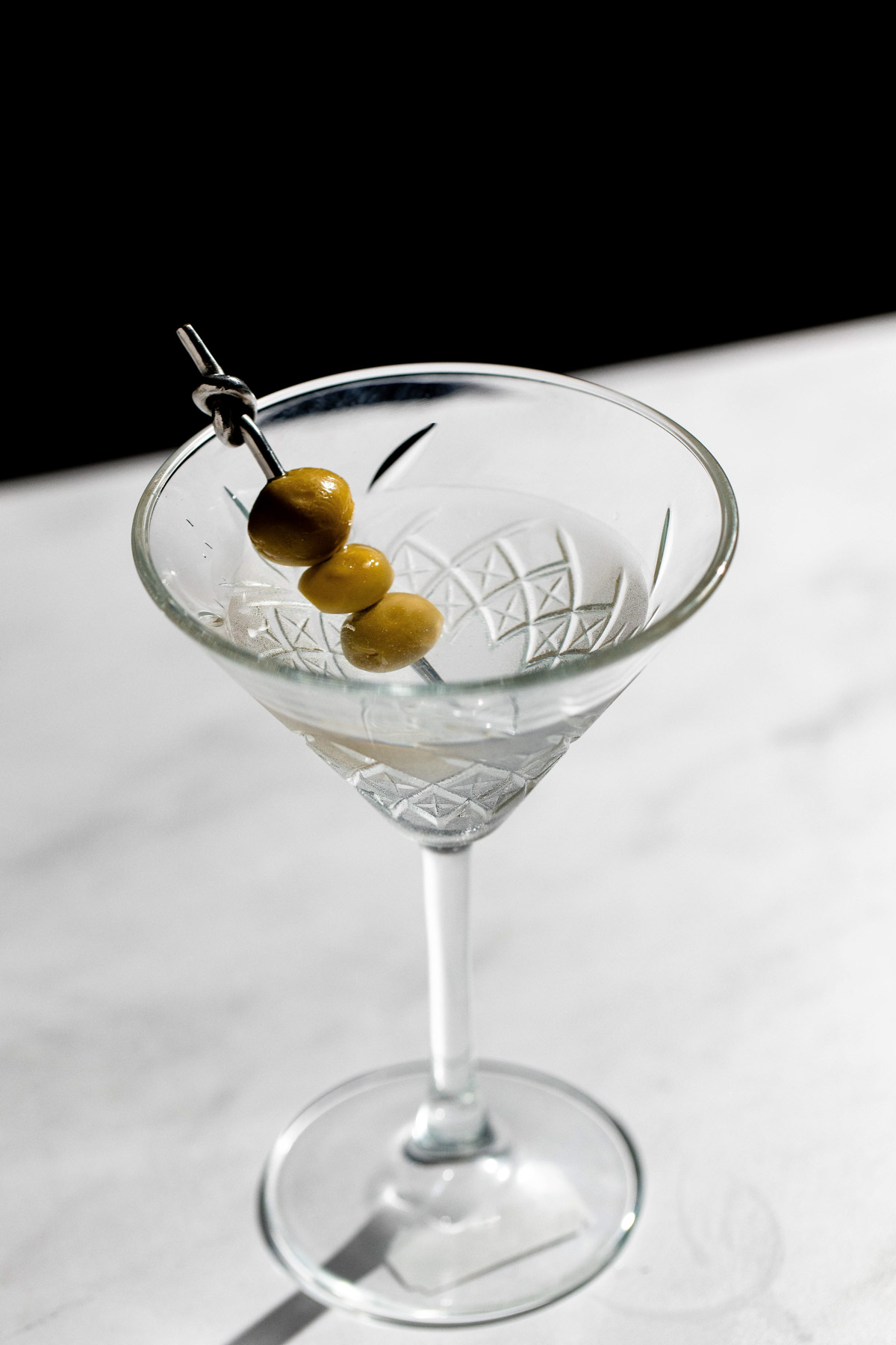 3 olives on a cocktail pick in a glass with a martini. 