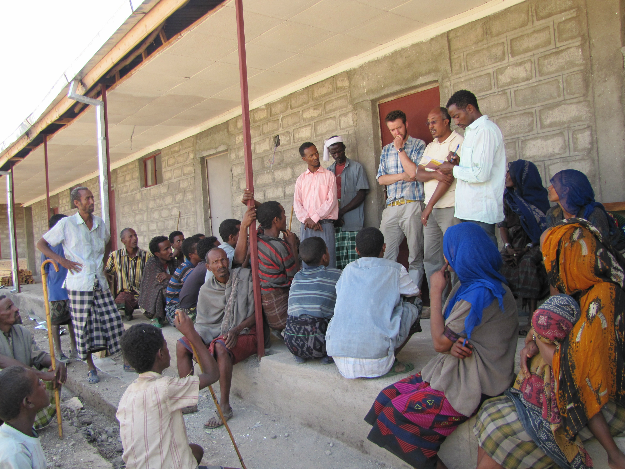 A few people stand in front of a building talking to a larger group of gathered people listening.