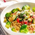 garlic pasta with veggies in a white bowl with parmesan cheese