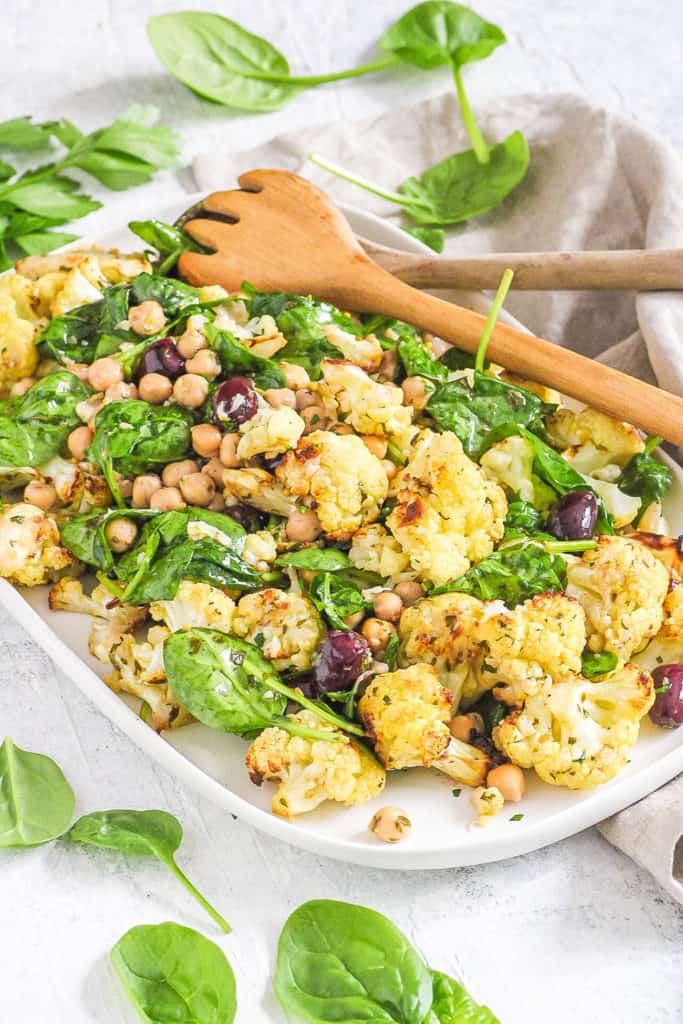 roasted cauliflower salad with spinach and chickpeas and kalamata olives, served on a white plate