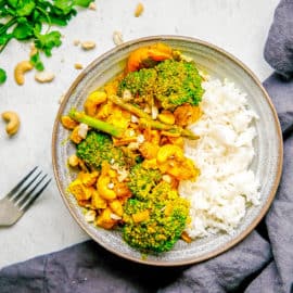 Tofu Yellow Curry with Veggies and Cashews served in a grey bowl with white rice