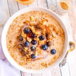 Pumpkin spice oatmeal with blueberries in a white bowl on a wooden countertop.