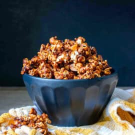 Black bowl overflowing with vegan caramel popcorn sitting on a yellow and white checkered towel.