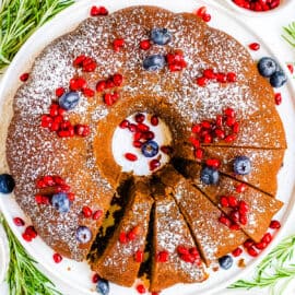 Gingerbread bundt cake topped with powdered sugar and fresh fruit on a white plate.