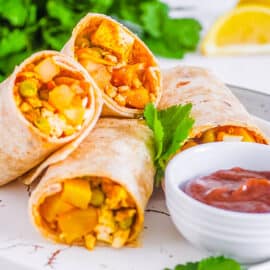 Indian samosa wraps cut in half and served on a white plate with chutney on the side.