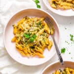 Creamy vegan mushroom pasta in a white bowl with a fork, topped with fresh herbs.