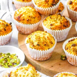 Homemade pistachio muffins stacked on a wooden cutting board.