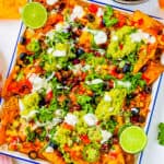 Loaded veggie nachos piled with veggies, jalapenos, guacamole, sour cream, cheese, olives served on a white platter.