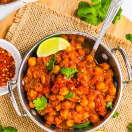 Chole masala served in a stainless steel bowl garnished with cilantro and lime.