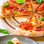 Poolish pizza dough topped with tomatoes and basil, baked in the oven and served on a wooden cutting board.