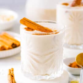 Vegan coquito served in a glass with a cinnamon stick as a garnish.