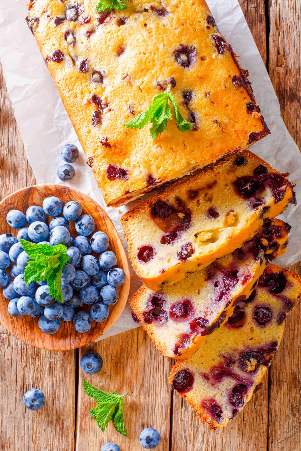 Blueberry banana bread, sliced on a wooden cutting board with fresh blueberries on the side.