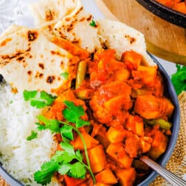 Vegetable vindaloo served in a bowl with naan and rice on the side.