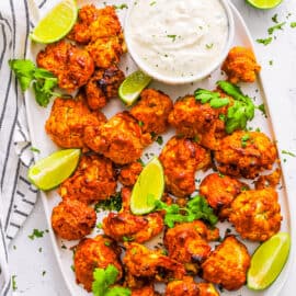 Tandoori cauliflower tikka arranged on a white plate with a yogurt dipping sauce on the side.