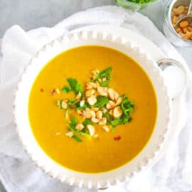 Curried cauliflower soup topped with crushed cashews and cilantro, served in a white bowl.