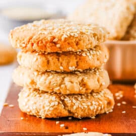 Sesame tahini cookies stacked on a wooden cutting board.